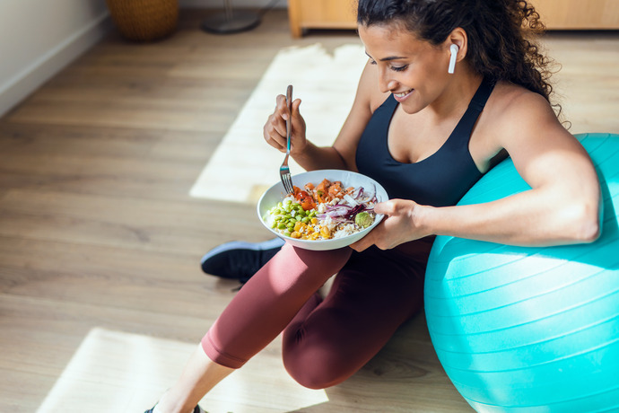 Mujer deportista comiendo un plato de vegetales apoyada sobre la pelota de pilates