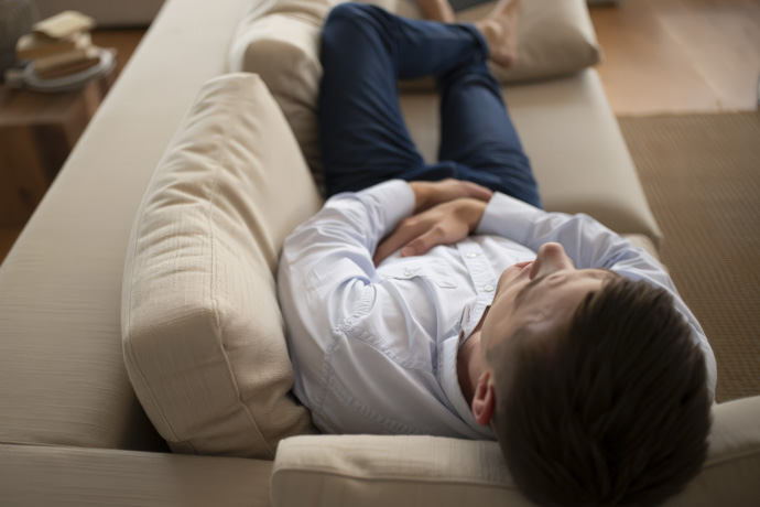Hombre recostado en un sofá con molestias abdominales relacionadas con efectos secundarios de la metformina
