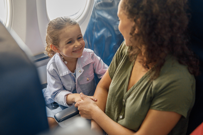 Mamá e hija en sus asientos en el avión, sonriendo