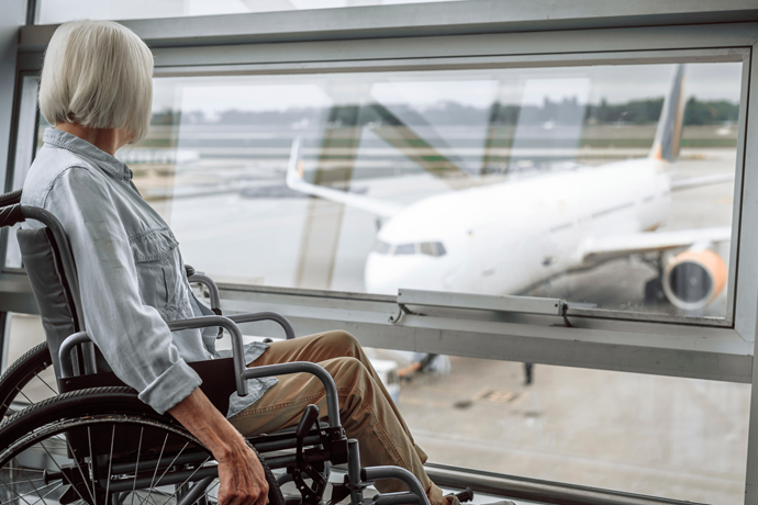 Mujer mayor en silla de ruedas, observando a avion desde ventana del aeropuerto