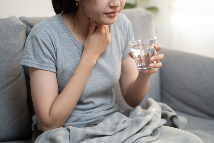 Mujer con dolor de garganta sujetando un vaso de agua