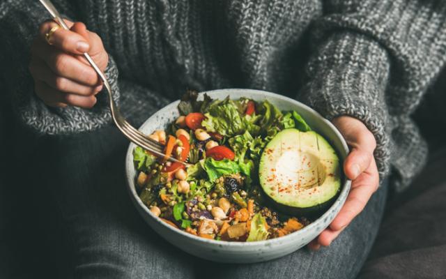 Woman holding plate of salad with avocado and vegetables