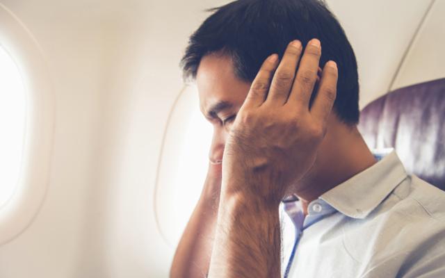 Hombre con dolor de oídos durante viaje en avión