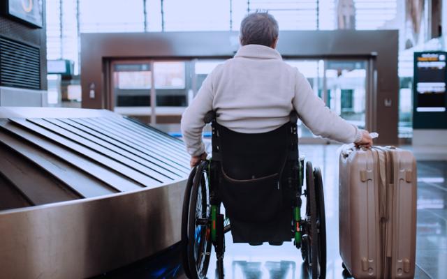 Hombre mayor en silla de ruedas, recogiendo su equipaje en el aeropuerto