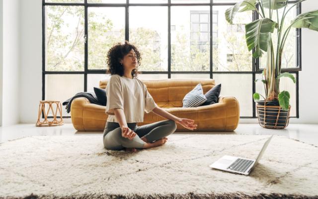 Mujer haciendo una meditación guiada con su computadora sobre una alfombra