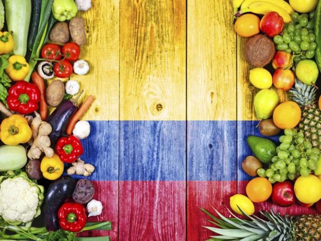 Variedad de frutas y verduras frescas con propiedades antiinflamatorias frente a la bandera de Colombia. 