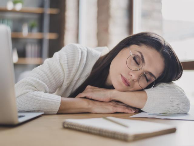 Mujer en Colombia descansando sobre su escritorio tras una jornada agotadora, reflejando las consecuencias de no dormir bien. 